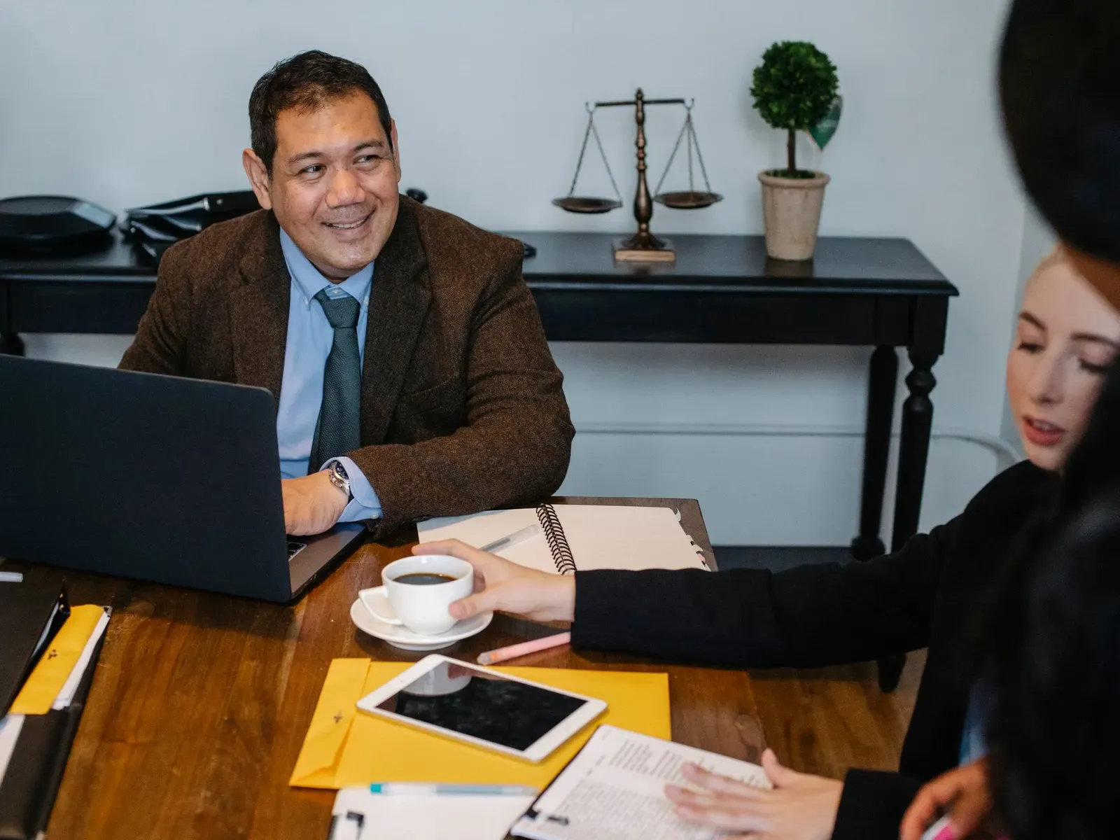A smiling man in a suit talking with a colleague across a desk in a law office