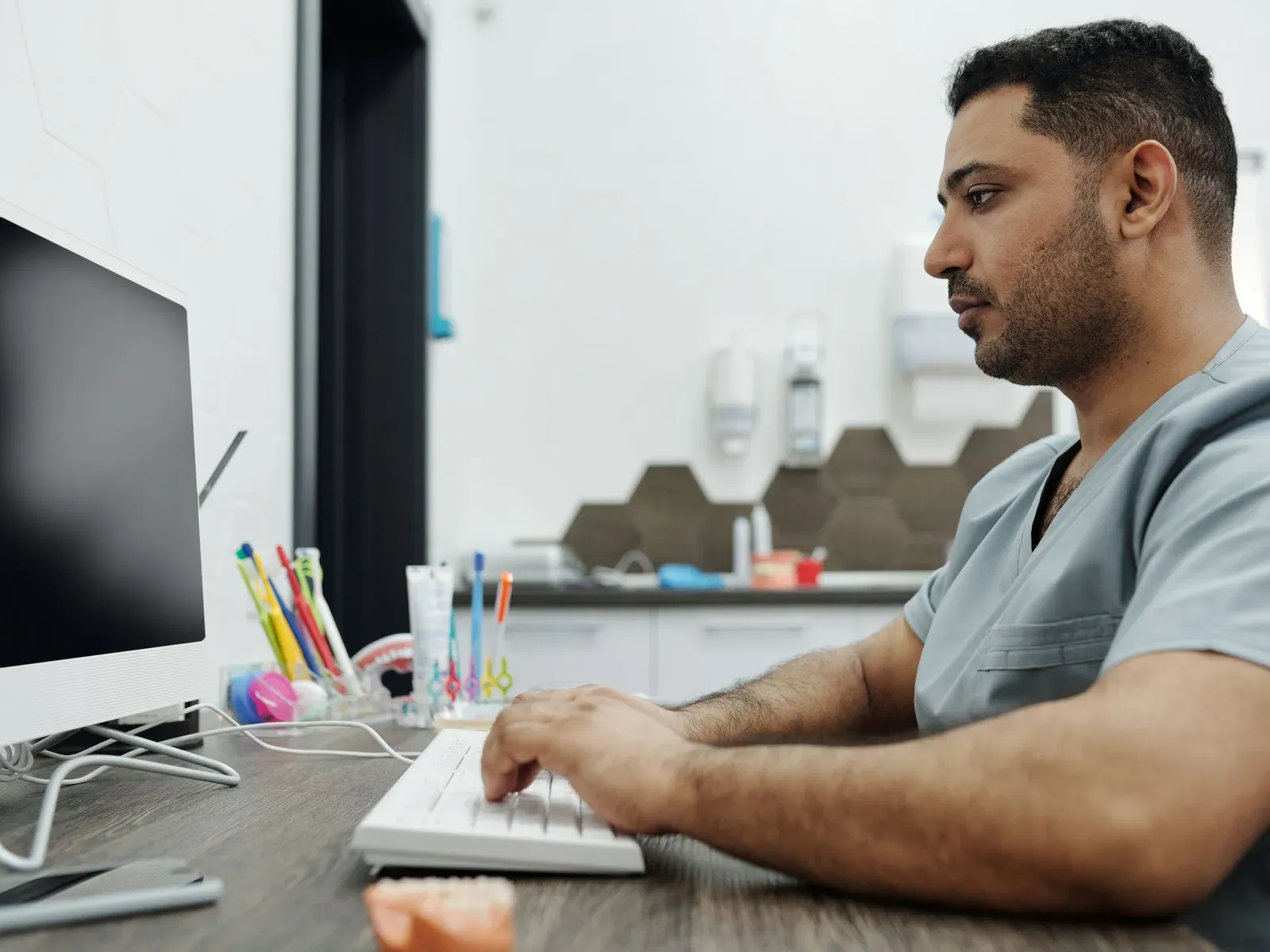 A dentist in scrubs typing at a computer in a dental office