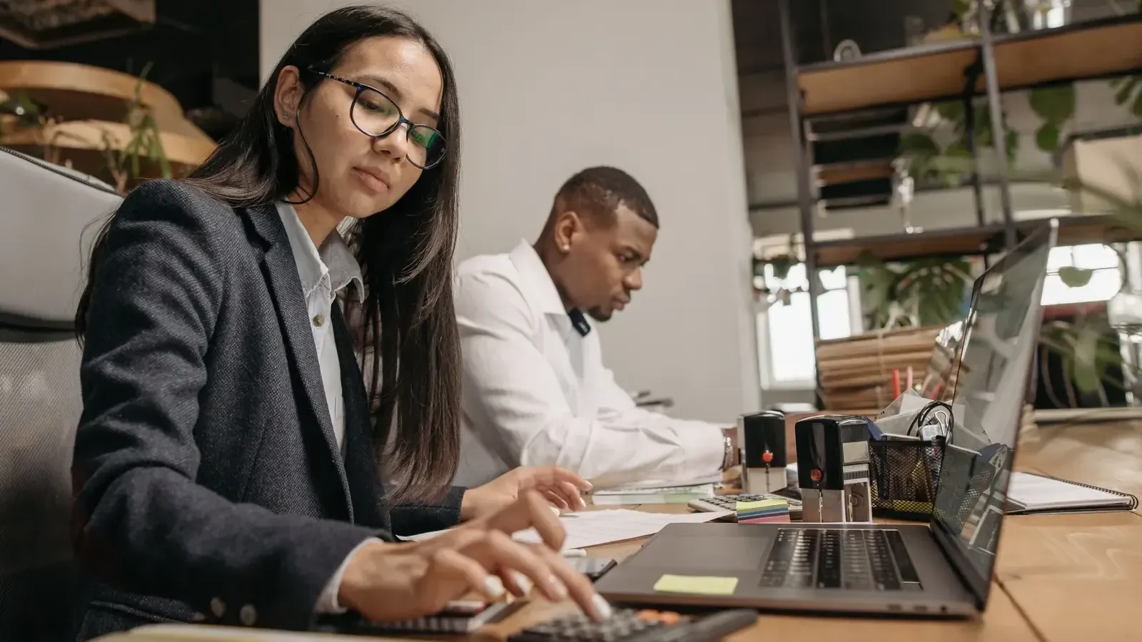 Two professionals working with laptops and calculators in a bright office
