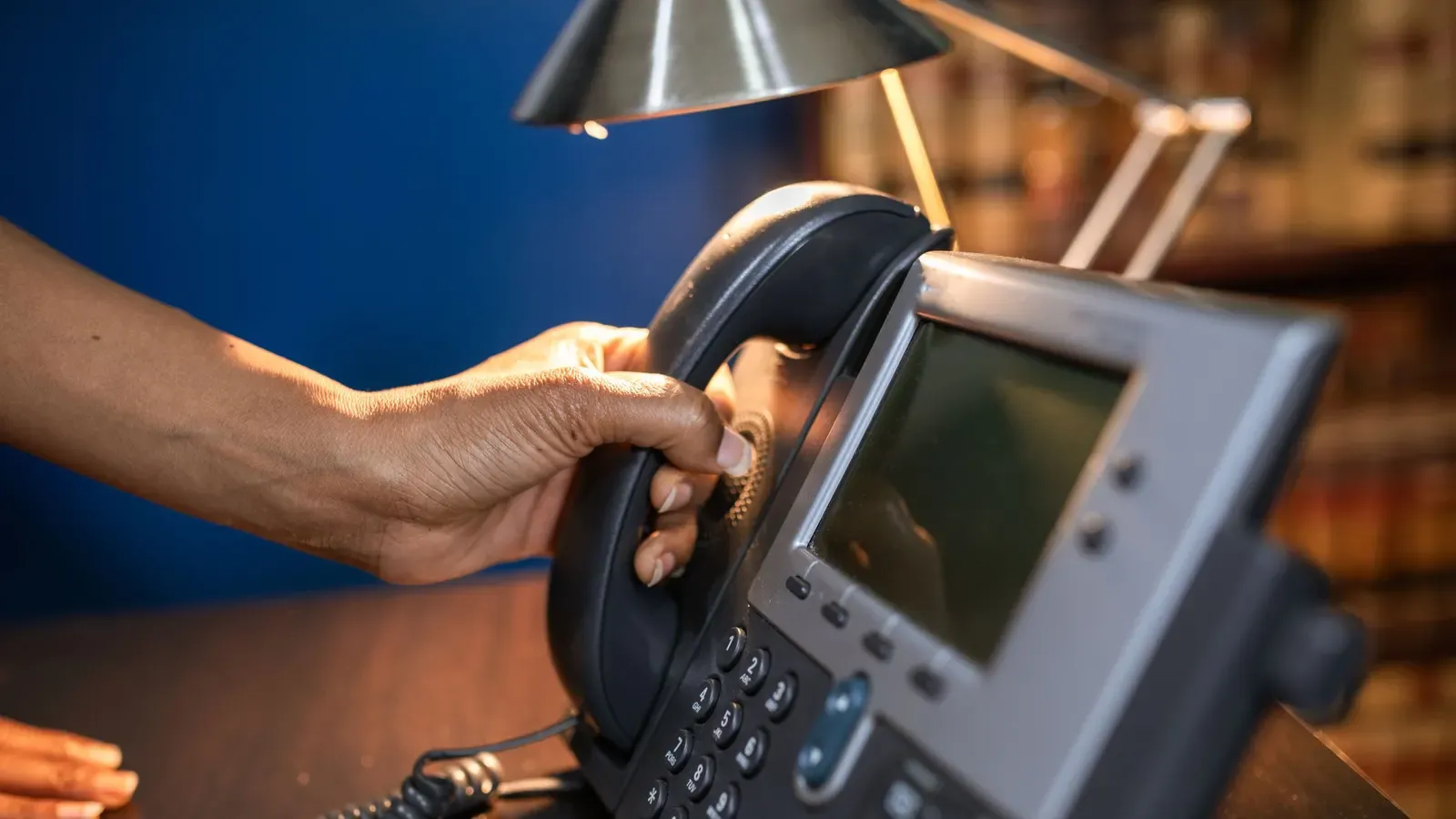 A hand lifting the handset of an IP desk phone