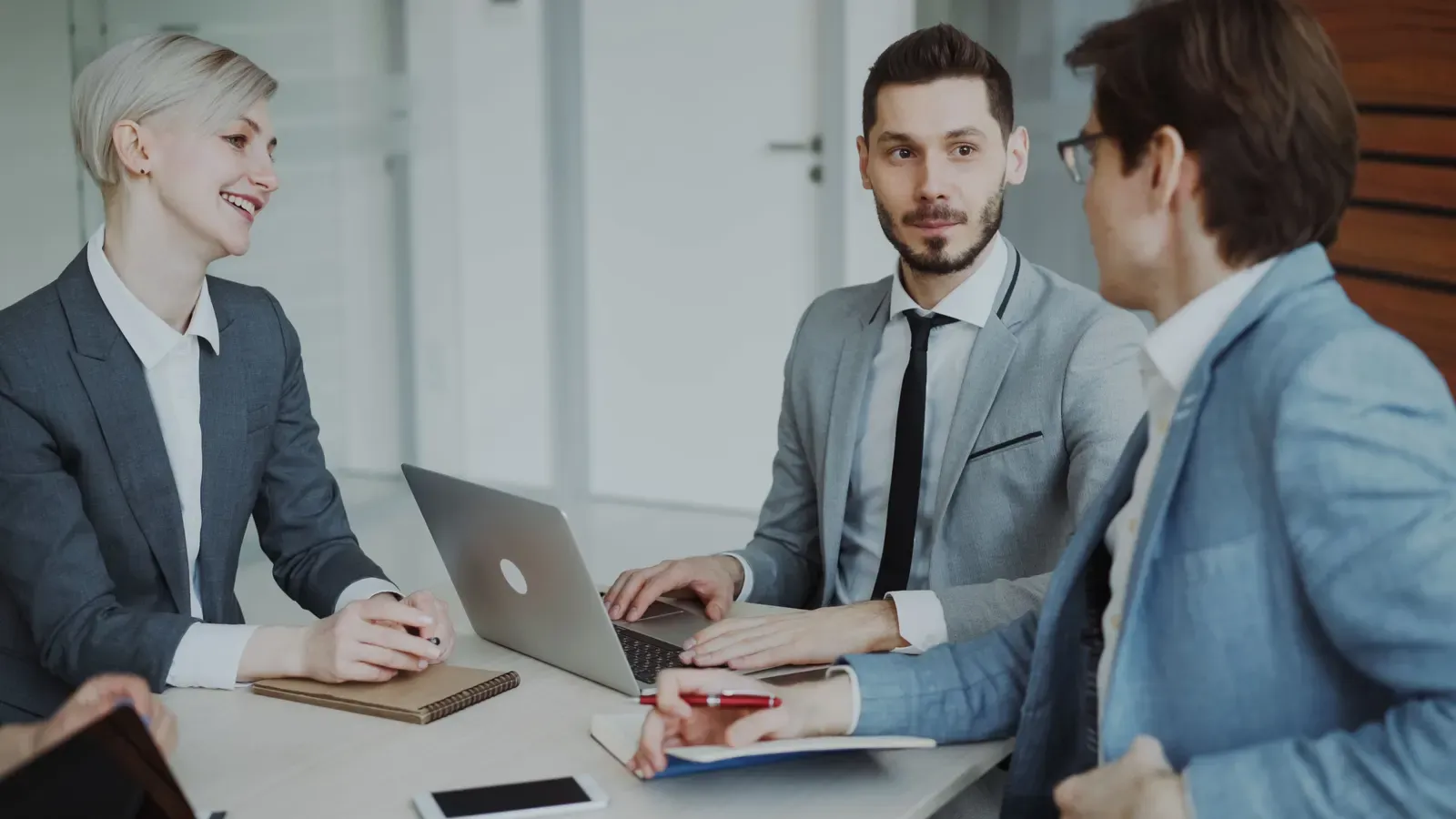 Three professionals in a meeting around a laptop in a bright office